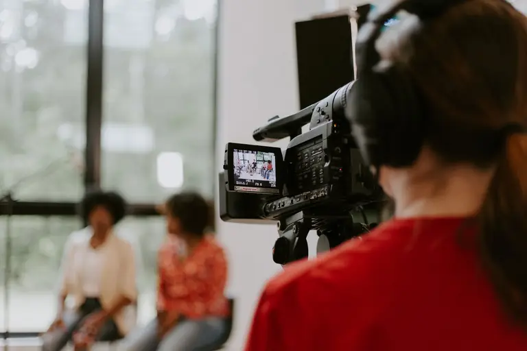 Camera operator filming a two-person interview in a bright studio